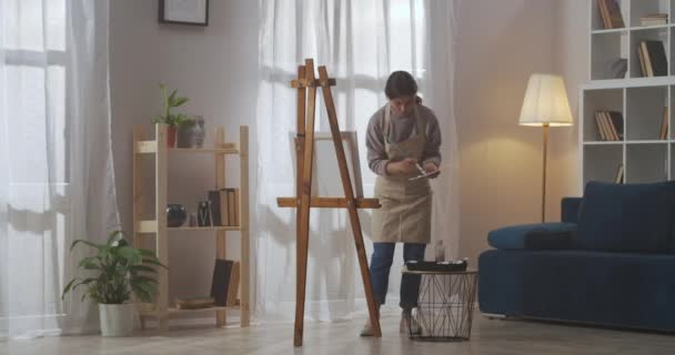 Νεαρή γυναίκα καλλιτέχνης χρησιμοποιεί σαλόνι του διαμερίσματος ως καλλιτεχνικό εργαστήριο για σχέδιο, χόμπι και επαγγελματικές δεξιότητες — Αρχείο Βίντεο