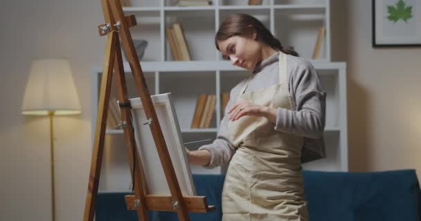 Jonge vrolijke vrouw tekent op doek op ezel in appartement 's avonds, hobby en favoriete tijdverdrijf — Stockvideo
