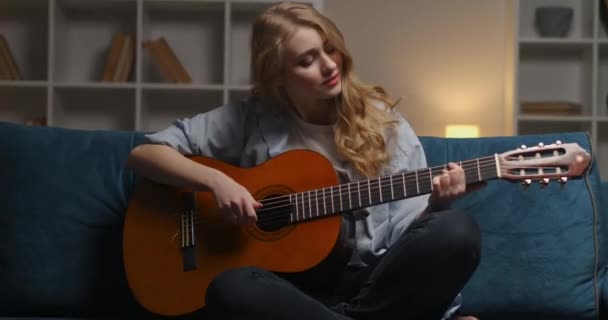 Новичок рок-музыкант женщина играет песню на акустической гитаре в квартире вечером, портрет счастливой эмоциональной леди — стоковое видео