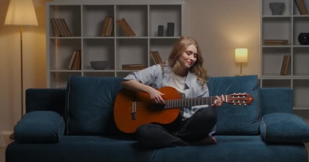 Iniciante músico feminino está compondo música tocando guitarra sentado em casa à noite — Vídeo de Stock