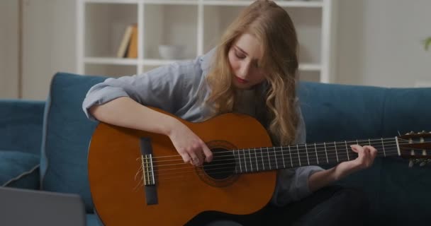 Jonge vrouw speelt melodie op gitaar, hobby en entertainment thuis in het weekend, zittend op de bank in de woonkamer — Stockvideo