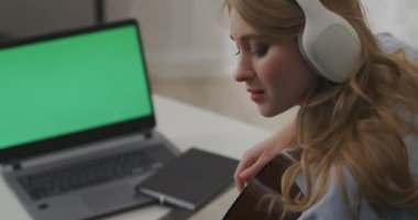 Güzel bayan müzisyen internet kamerasının önünde gitar çalıyor, evden online yayın konseri, yeşil ekran.