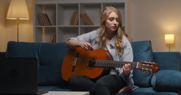 Przemyślana młoda kobieta gra smutną piosenkę na gitarze wieczorem w domu, kreatywne hobby i rozrywka, romantyczny nastrój — Wideo stockowe