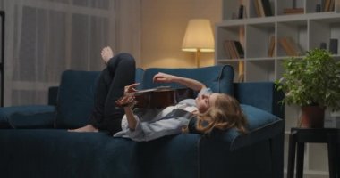 Kadın akşamları evde dinleniyor, akustik gitar telleri çalıyor, hüzünlü duygular ve melankoli hissediyor.