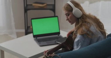 Genç kadın internette gitar çalmayı öğreniyor, masadaki yeşil dizüstü bilgisayar ekranı, kendini eğitme