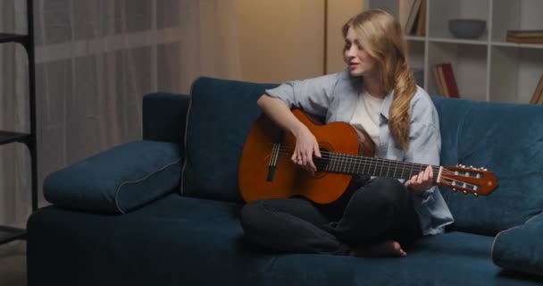 Szczęśliwa emocjonalna kobieta gra na gitarze siedzi sama w salonie nowoczesnego mieszkania w godzinach wieczornych, portret kobiety muzyk — Wideo stockowe