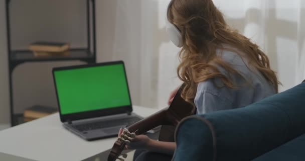 Teenager-Mädchen benutzt Selbsthilfeanleitung zum Gitarrespielen am Laptop, Saiten zupfen, am Wochenende allein zu Hause sitzen — Stockvideo