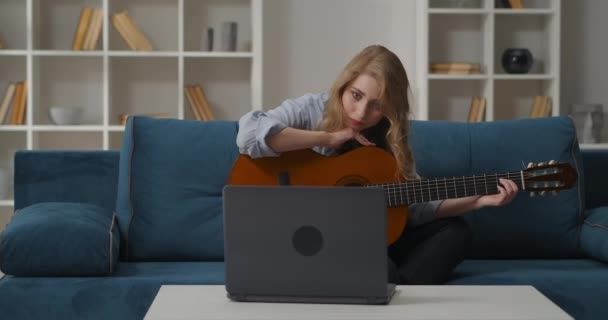 Teen girl is learning to play on guitar, προβολή φροντιστήριο στο διαδίκτυο από το laptop, παίζοντας συμφωνίες σε χορδές — Αρχείο Βίντεο