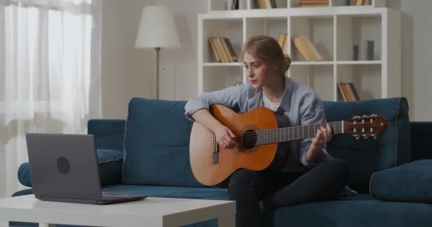 10 대 소녀가 거실에서 기타를 치며 인터넷으로 배우는 영상을 보고 있습니다. 여성 초심자 음악가 — 비디오