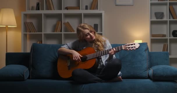 Pasar la noche sola en casa, mujer joven está tocando la guitarra y disfrutando de la música, arrancando cuerdas — Vídeo de stock