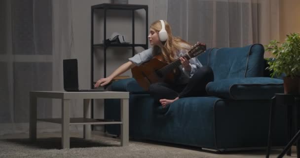 Kvinnlig nybörjare musiker sitter med akustisk gitarr på blå soffa i vardagsrummet i modern lägenhet — Stockvideo