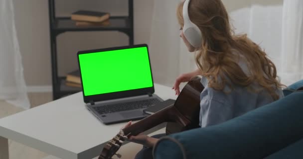 Donna sta provando la canzone alla chitarra in appartamento, seduto di fronte al computer portatile con display verde e suonare, strappare le corde — Video Stock