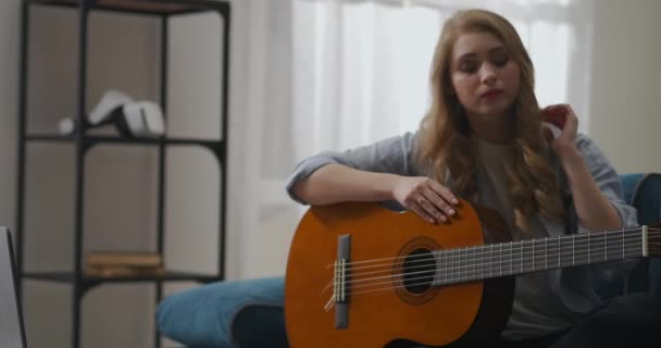 Mujer está aprendiendo a tocar la guitarra por Internet, descansando en casa, comunicarse con el tutor por chat de vídeo en el ordenador portátil, pasatiempo — Vídeo de stock