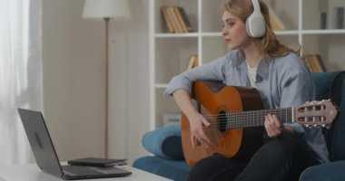 Kadın müzisyen evde gitar çalıyor, kulaklıkla müzik dinliyor, hafta sonları tek başına vakit geçiriyor.