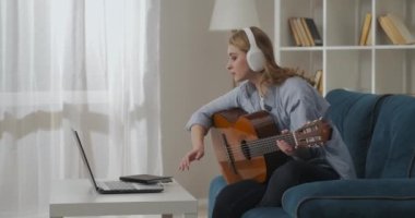 Kadın dizüstü bilgisayarda şarkı seçiyor ve gitarla melodi çalıyor. Hafta sonu dairede koltukta oturuyor.