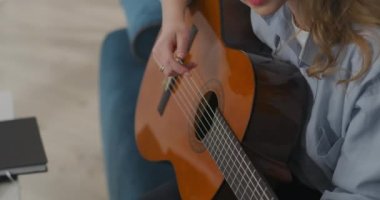 Genç bir kadın müzik yapıyor, dairede gitar çalıyor, yeşil dizüstü bilgisayara, krom anahtar teknolojisine bakıyor.