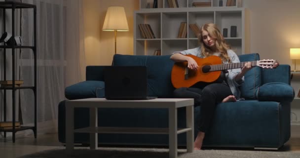 Beginner female musician is plucking strings of guitar, learning to play at evening, composing new song — Stock Video