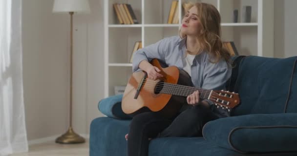Feliz joven mujer está tocando la guitarra en casa en fin de semana, pasar tiempo en la sala de estar, haciendo música, pasatiempo — Vídeos de Stock