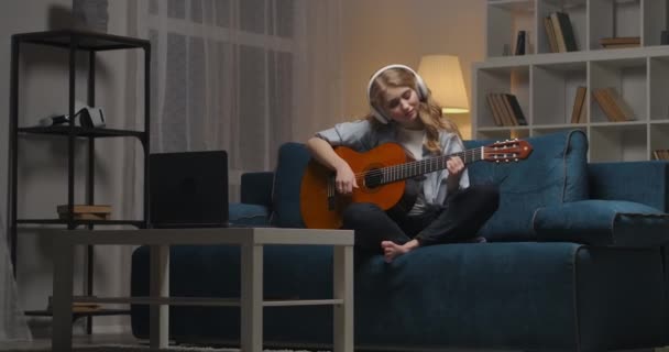 Vrolijke vrouw is het hebben van plezier alleen thuis 's avonds, gitaar spelen en ontspannen in gezellig appartement — Stockvideo