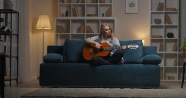 Genç ve yetenekli bir kadının hobisi ve tutkusu, bayan akşam evde gitar çalıyor, favori şarkının tadını çıkarıyor.