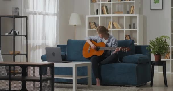 Muziek liefhebber vrouw speelt gitaar in de woonkamer, het bekijken van notities en akkoorden op internet, tijd doorbrengen in het weekend — Stockvideo