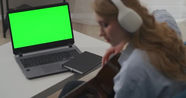 Jovem está tocando guitarra sentado na frente do laptop com tela verde, concepção de guia de auto-ajuda ou ensaio on-line — Vídeo de Stock