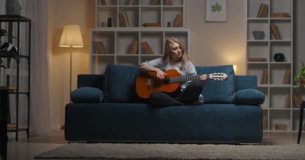 젊은 재능있는 여자의 취미와 열정, 여자는 저녁에 집에서 기타를 치며 좋아 하는 노래를 즐긴다 — 비디오