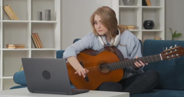 Ung kvinna lär sig ny sång på gitarr i vardagsrummet i lägenhet, ha kul på helgen, visning handledning i internet, nybörjare sångare och musiker — Stockvideo