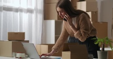 Meşgul iş kadını cep telefonuyla konuşuyor, notlar yazıyor, bir sürü karton kutuyla ev deposunda çalışıyor.