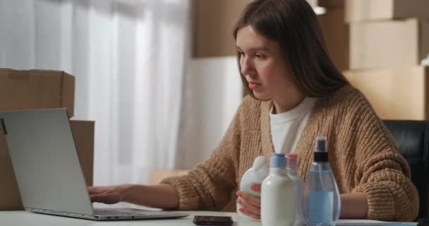 Γυναίκα εργάζεται σε μικρή εταιρεία εμπορίας ή παραγωγής οικιακών χημικών ουσιών, συμπληρώνοντας πληροφορίες σχετικά με τα προϊόντα σε φορητό υπολογιστή, μέσο πορτρέτο — Αρχείο Βίντεο