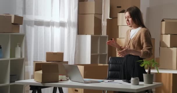 Онлайн зустріч партнерів за допомогою відеочату в ноутбуці, жінка говорить зі складу з багатьма картонними коробками, невеликою компанією — стокове відео