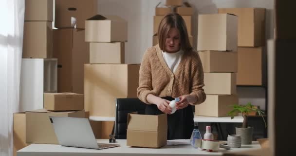 Femme est une commande d'emballage avec des cosmétiques faits à la main dans une boîte en carton dans un petit entrepôt à la maison, une entreprise et l'esprit d'entreprise — Video