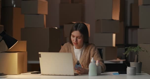 Overuren in magazijn, vrouwelijke specialist werkt 's avonds met laptop, bestudeert nieuwe cosmetische producten, gebruikt laptop met internet — Stockvideo