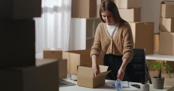 Γυναίκα εργαζόμενος βάζει χειροποίητα καλλυντικά στο κουτί για τον πελάτη, την προετοιμασία των προϊόντων για την παράδοση στην αποθήκη σπίτι, ιδιοκτήτης της μικρής επιχείρησης — Αρχείο Βίντεο