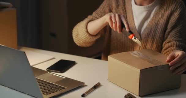 Ung kvinna packar upp låda med kosmetika från leveransservice, sitter vid bordet på kvällen i rum av lägenhet eller kontor — Stockvideo
