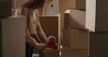 Kadın, el yapımı ürünleri çevrimiçi satarak, ev deposunda rulo kasetçalarla kutuları mühürlüyor.