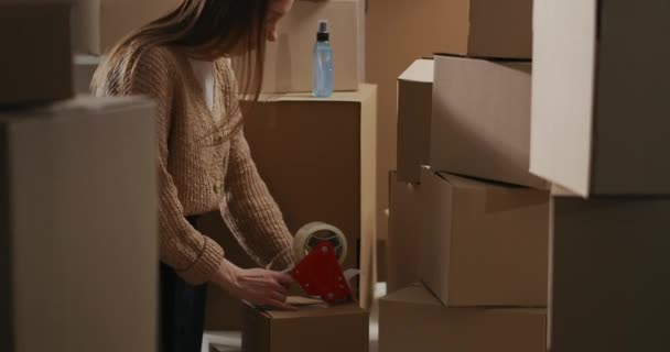 Donna sta sigillando scatola con merci da roll-on tape dispenser nel magazzino domestico, il commercio di prodotti fatti a mano online — Video Stock