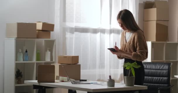 Kvinna som arbetar i små leveransföretag ringer till kund eller partner via mobiltelefon, logistikavdelning — Stockvideo