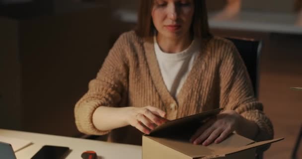 Volwassen vrouw is verpakking doos met cosmetische voor de levering, zitten aan tafel 's avonds in de kamer van appartement of kantoor — Stockvideo