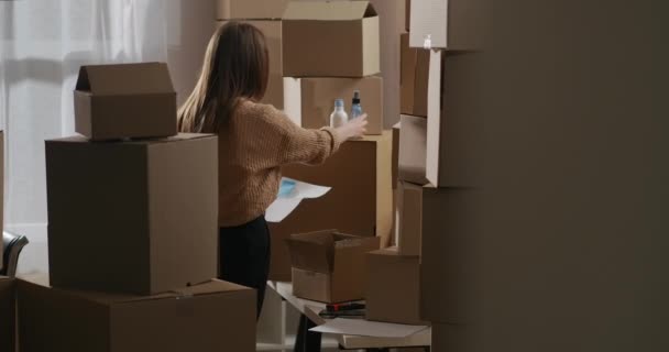 Mulher está desempacotando caixas com cosmético para o comércio, verificando bens no armazém home, documento de leitura, empresa de pequeno porte — Vídeo de Stock