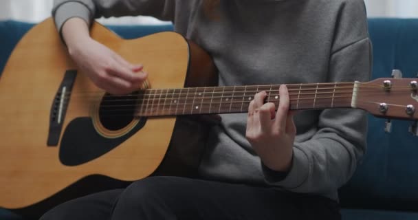 Seorang gadis muda sedang mempelajari akord untuk bermain gitar sambil duduk di sofa di kamarnya. Tembakan jarak dekat. — Stok Video