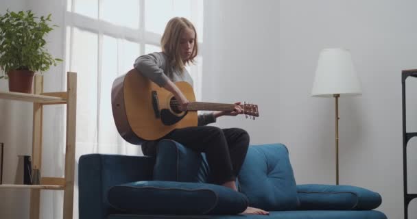 Una giovane ragazza con i capelli biondi si sta godendo la sua melodia su una chitarra acustica con una bella luce del sole in una stanza bianca. Lungo corto. — Video Stock