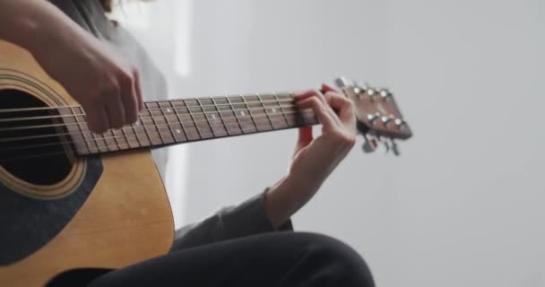 Un adolescente con ropa de casa toca la guitarra solo. La mujer compone música en el interior. El artista toca una hermosa guitarra. La chica entrena en un instrumento musical. Primer plano de disparo. — Vídeo de stock