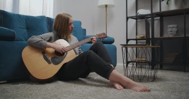 Gyönyörű nő ül a padlón a szobában. A lány elszigetelten tanul meg hangszeren játszani. Egy diák online leckét néz egy laptopon.. — Stock videók