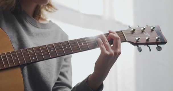 Um adolescente toca guitarra em uma sala de estar branca com luz solar. A mulher compõe música dentro de casa. O artista toca guitarra clássica. Uma menina está praticando um instrumento musical sozinha durante uma pandemia. — Vídeo de Stock