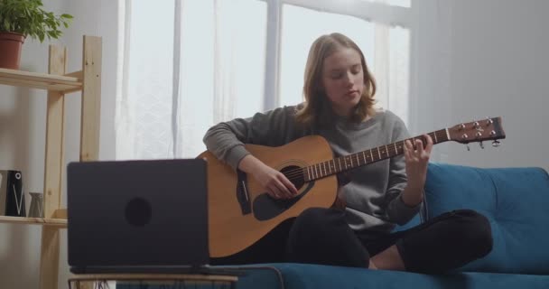 Kız odada dizüstü bilgisayarın önünde gitar çalıyor.. — Stok video
