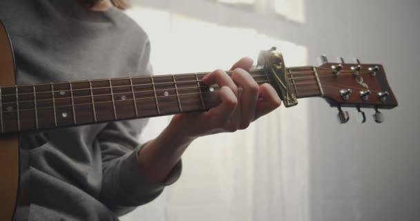 Підліток у домашньому одязі грає на гітарі. Жінка створює спокійну музику у світлій кімнаті. Художник грає на гітарі. Дівчина тренується на музичному інструменті. Крупним планом постріл . — стокове відео