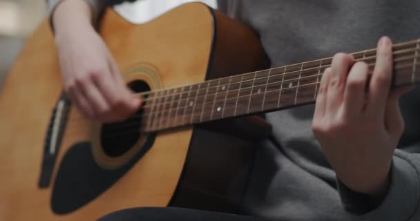 Een tiener leert thuis na school nieuwe akoestische gitaarakkoorden. Close-up opname. — Stockvideo