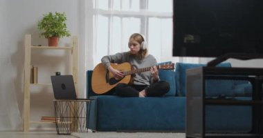 Kulaklıklı kız evde gitar çalmayı online bir öğretmenin yardımıyla öğreniyor.
