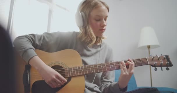 Mutlu genç kız sol eliyle bir gitar akoru tutuyor. Kulaklıklı bir kadın müzik dinliyor.. — Stok video